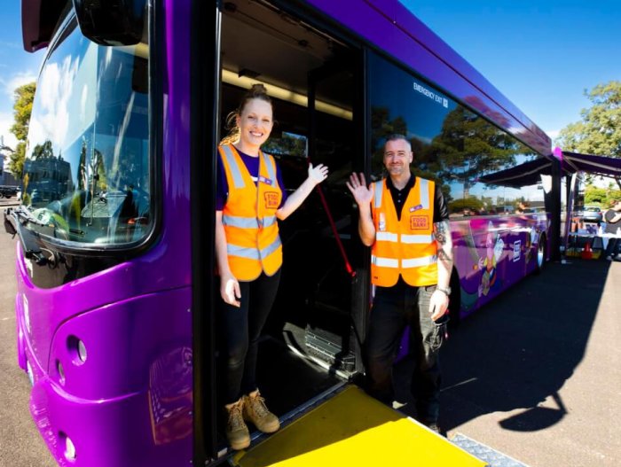 Foodbank volunteers standing outside purple mobile supermarket bus waving